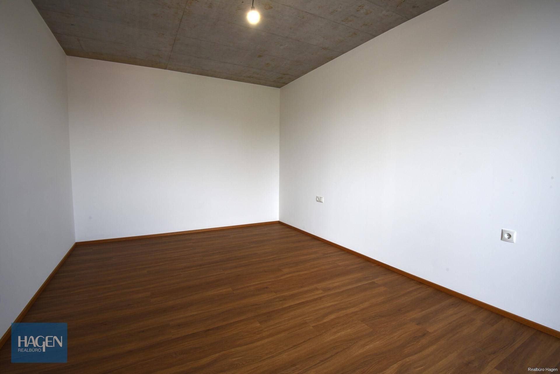 Schlichter Raum mit Laminatboden und weißen Wänden, ideal als Schlaf- oder Arbeitszimmer.