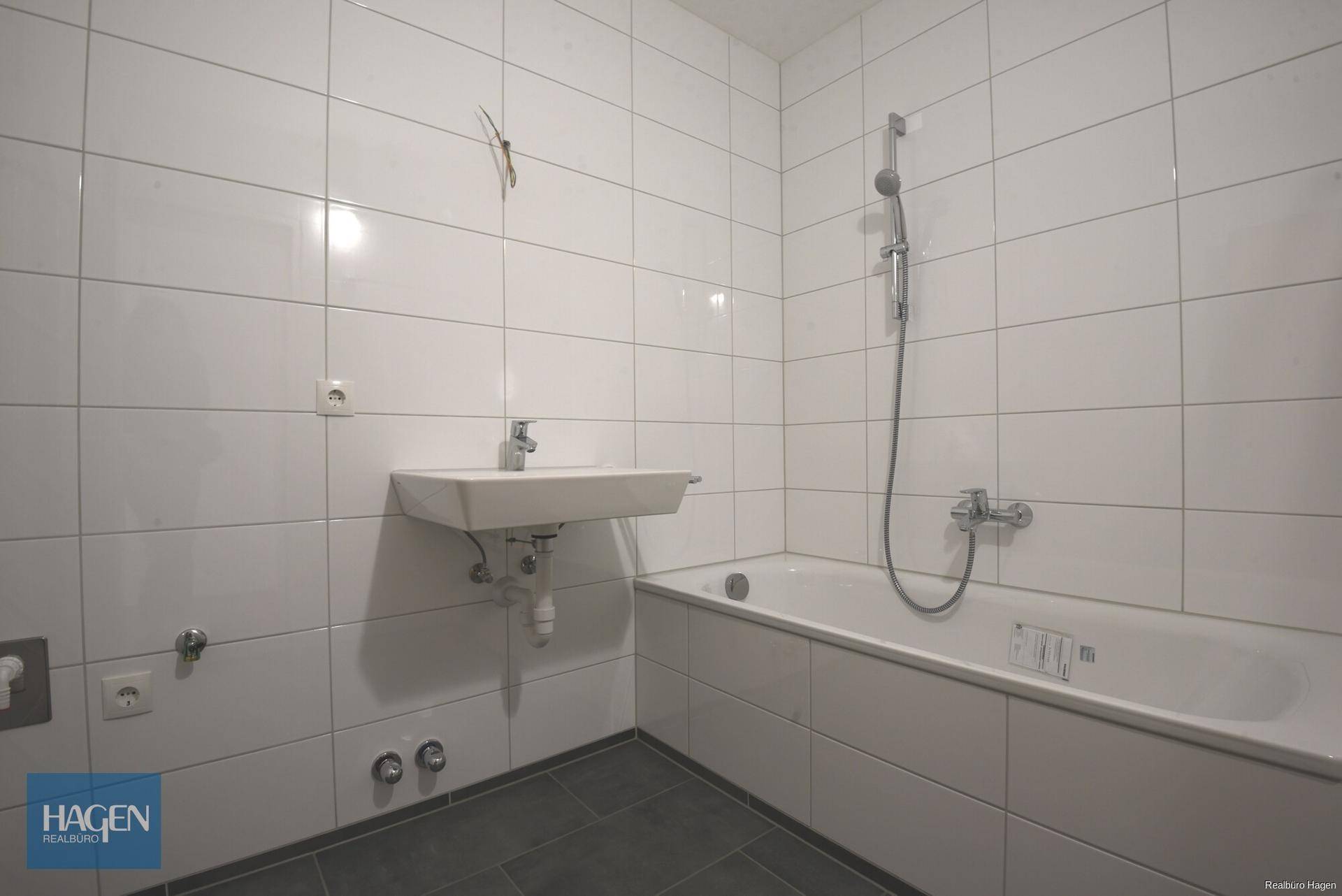 Gefliestes Badezimmer mit Badewanne und Waschbecken, bereit für die Endinstallation der Armaturen.