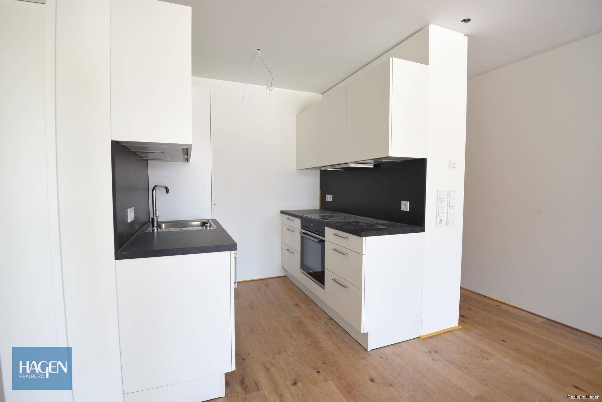 Moderne, ungenutzte Küche mit weißen Schränken, dunkler Arbeitsplatte und Holzboden.