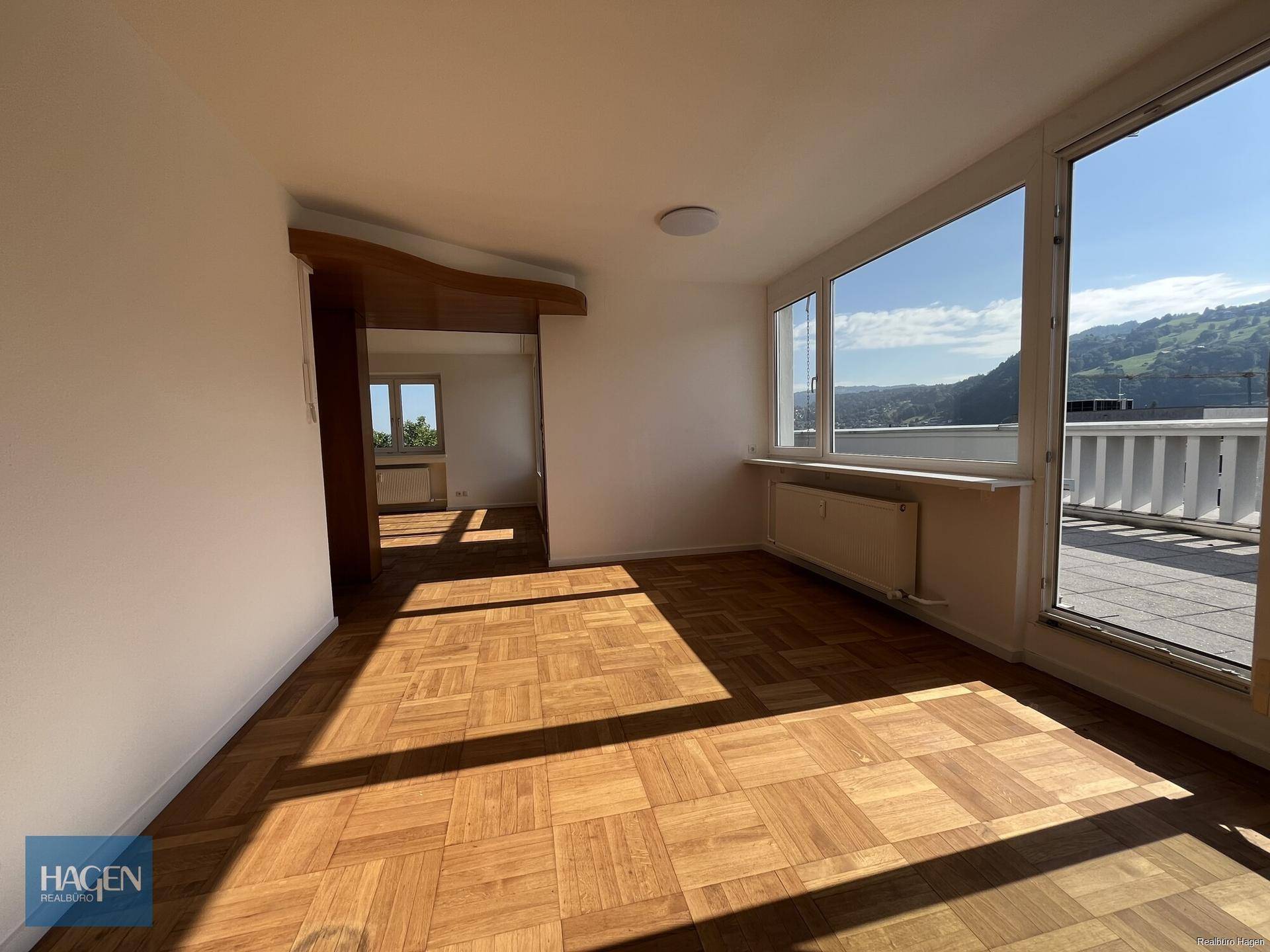 Lichtdurchfluteter Raum mit Parkettboden und Zugang zu einer großen Terrasse mit Panoramablick.
