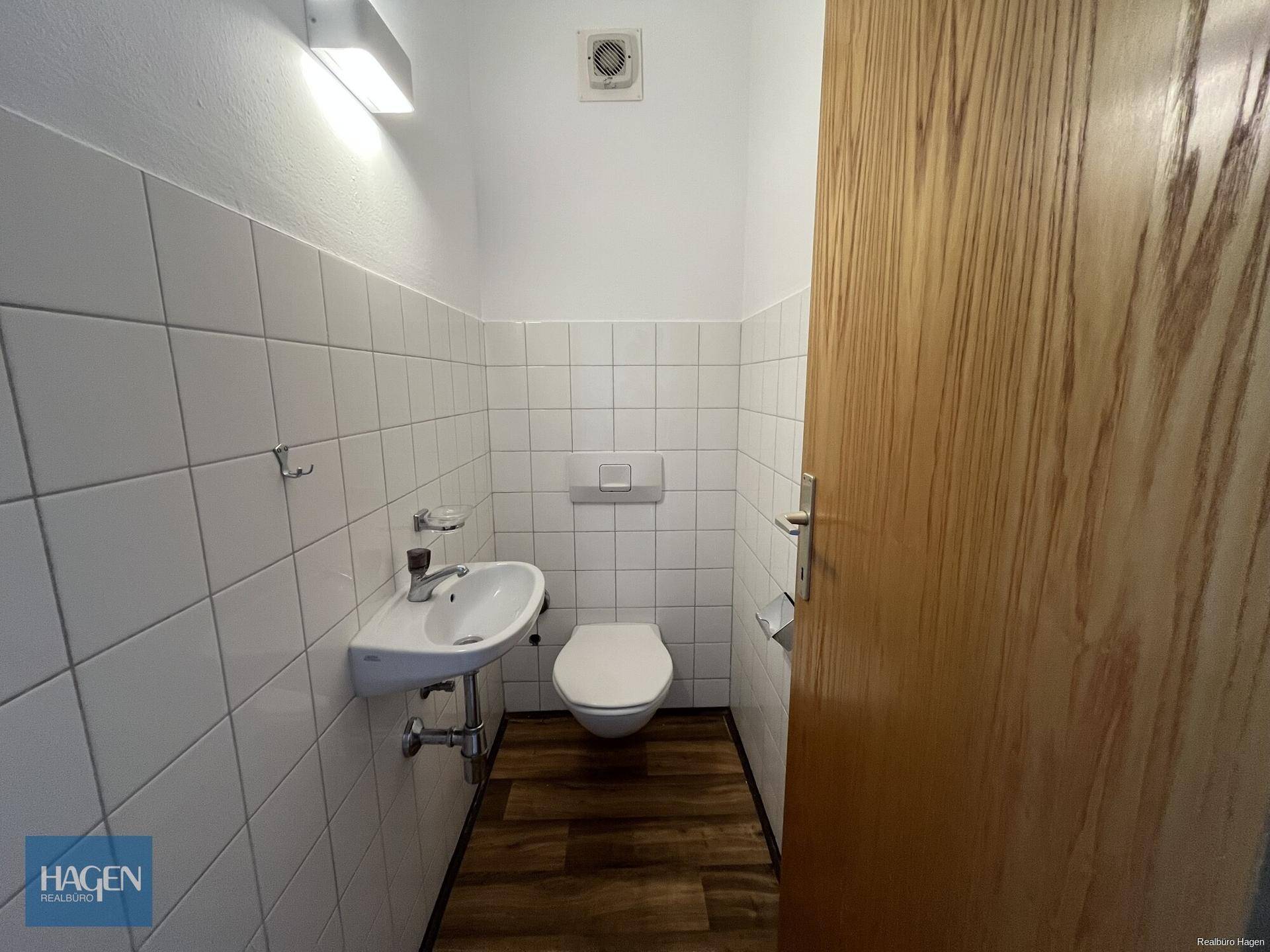 Kleines Gäste-WC mit weißen Fliesen, wandhängendem WC und Waschbecken.
