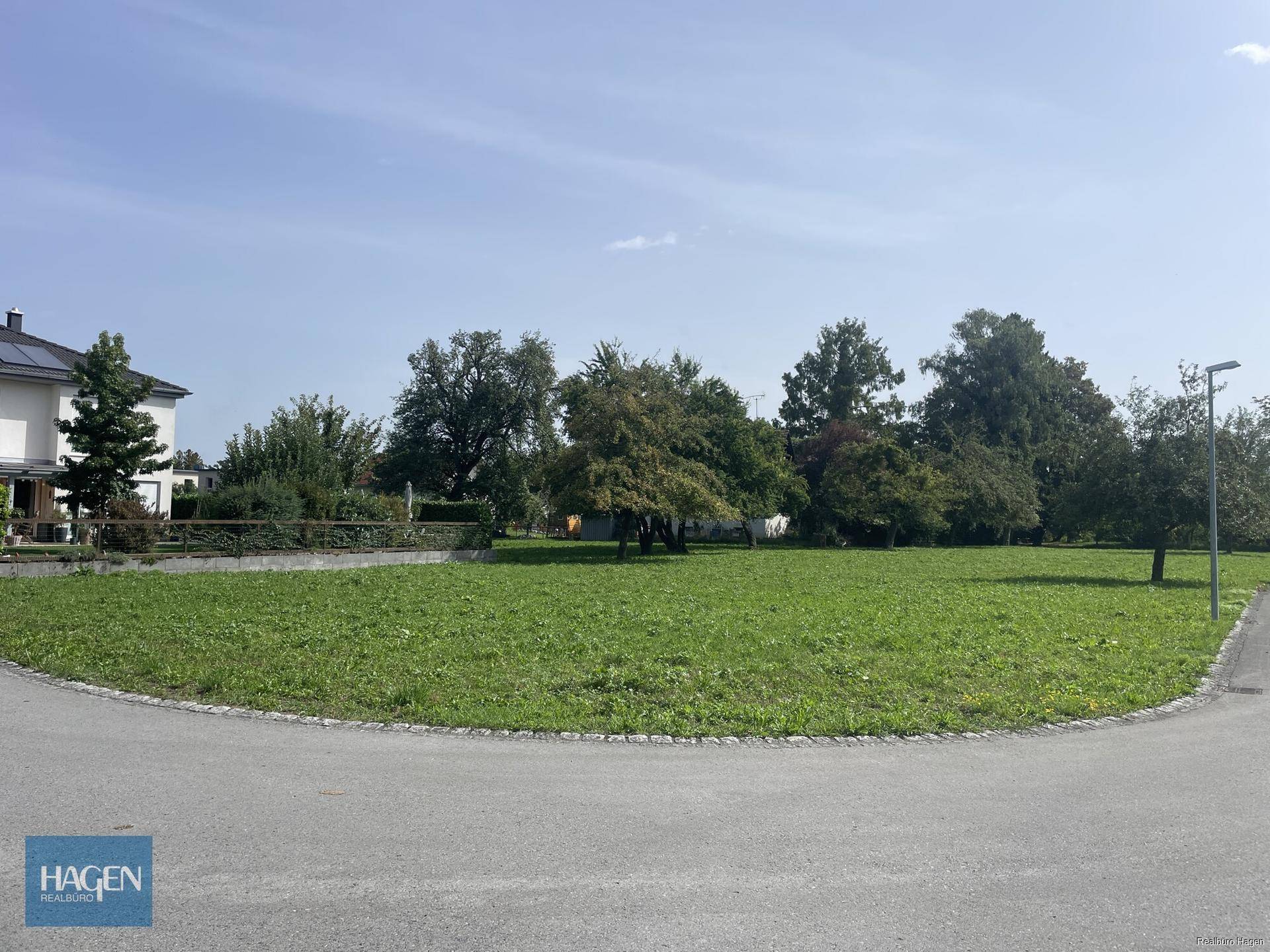 Grünes Grundstück mit angrenzender Straße und umliegender Wohnbebauung unter klarem Himmel.