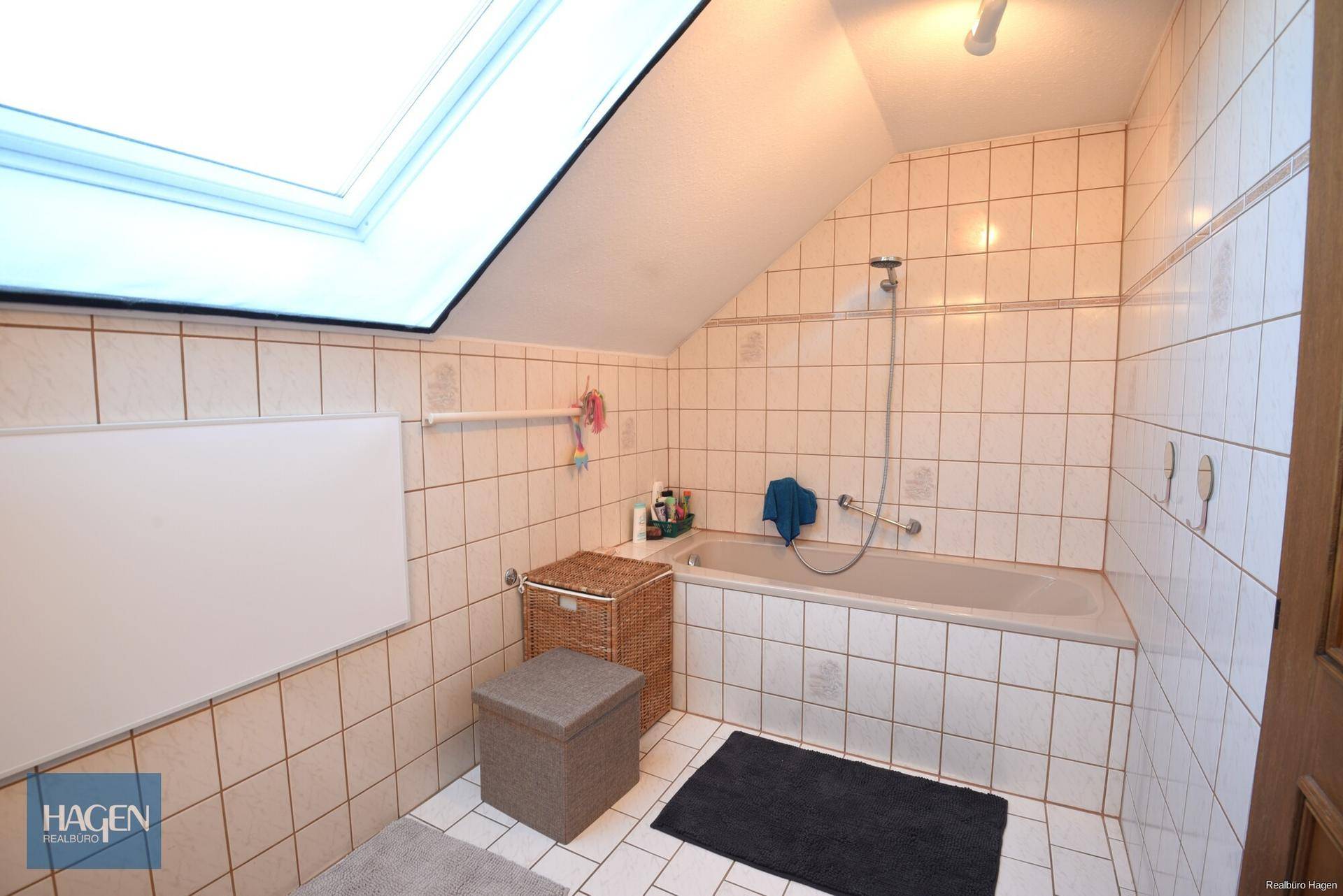Badezimmer im Dachgeschoss mit Badewanne, Dachfenster und hellen Fliesen.
