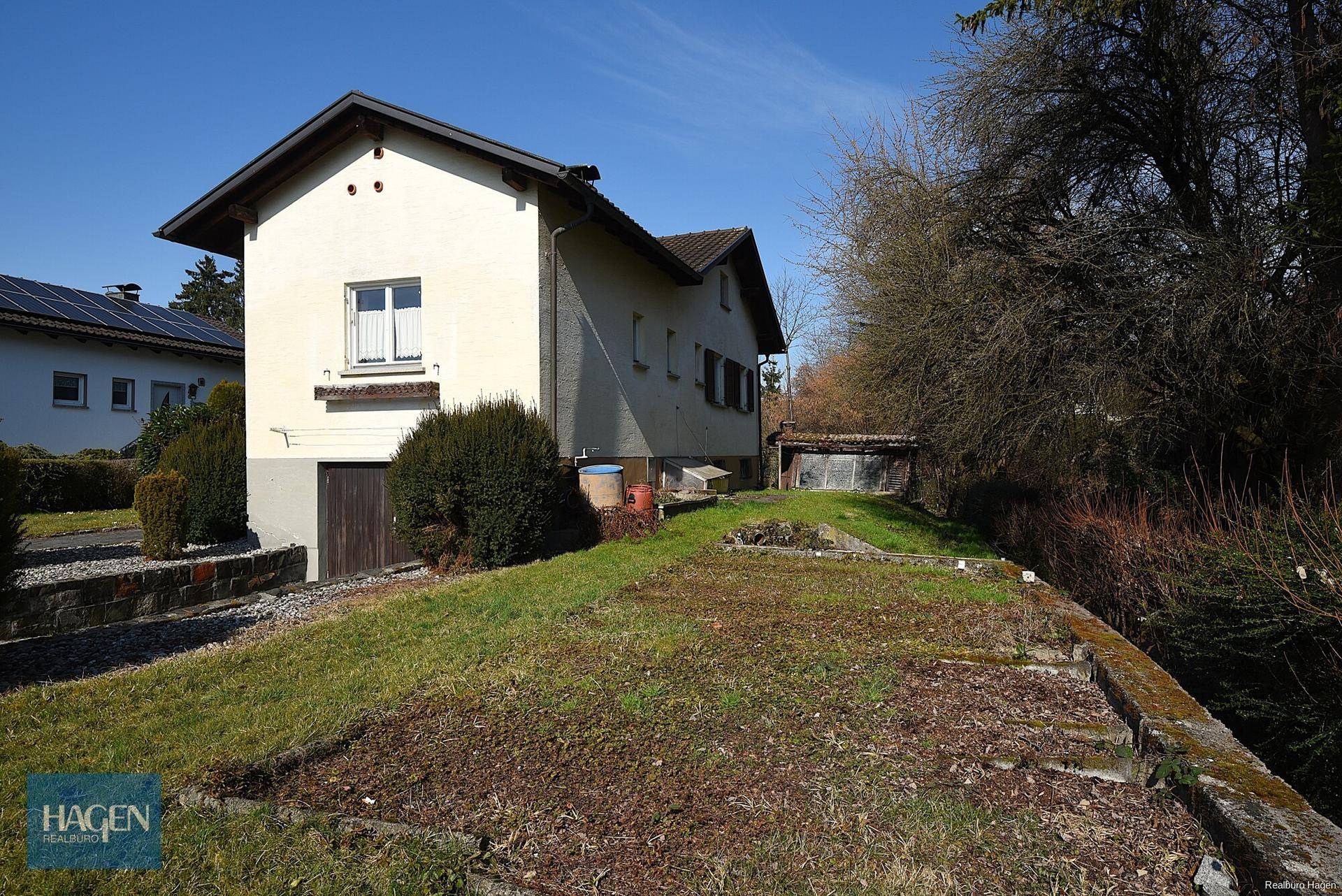 Seitenansicht des Hauses mit Gartenbereich, Rasenfläche und einem kleinen Schuppen im Hintergrund.