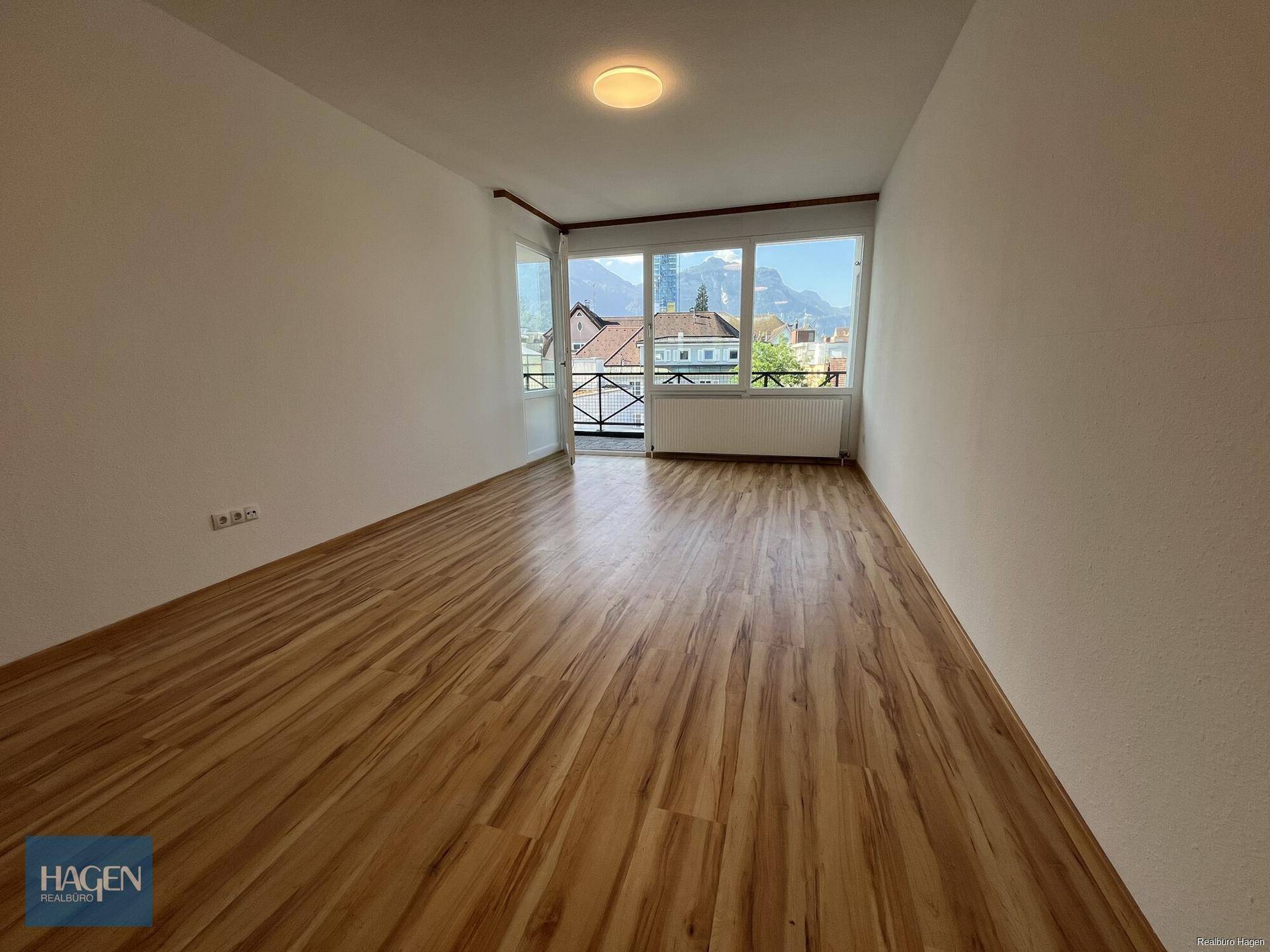 Geräumiges Zimmer mit Laminatboden, großen Fenstern und Zugang zu einem kleinen Balkon mit Bergblick.