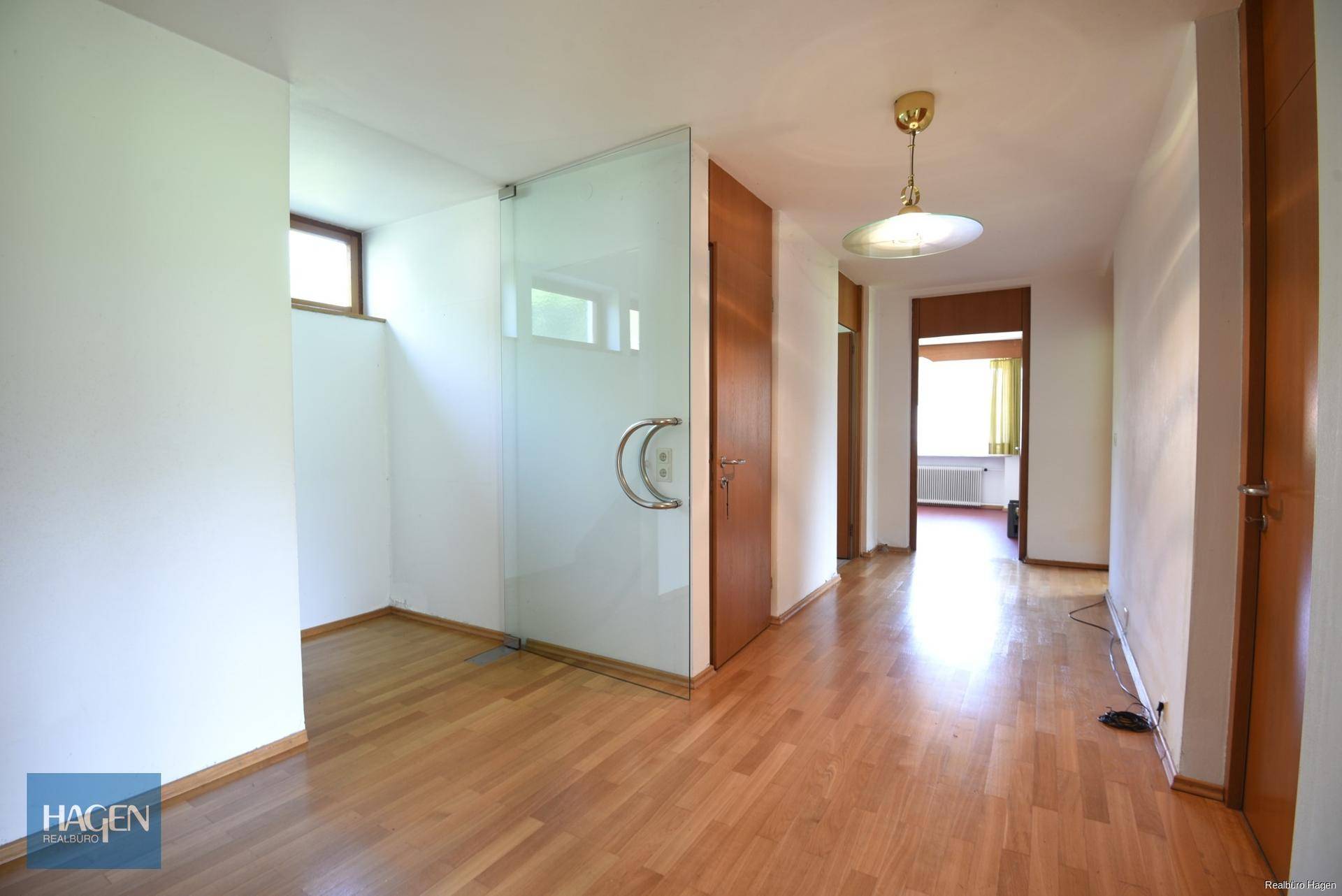 Heller Flur mit Holzboden und Glastür, der zu weiteren Räumen führt.