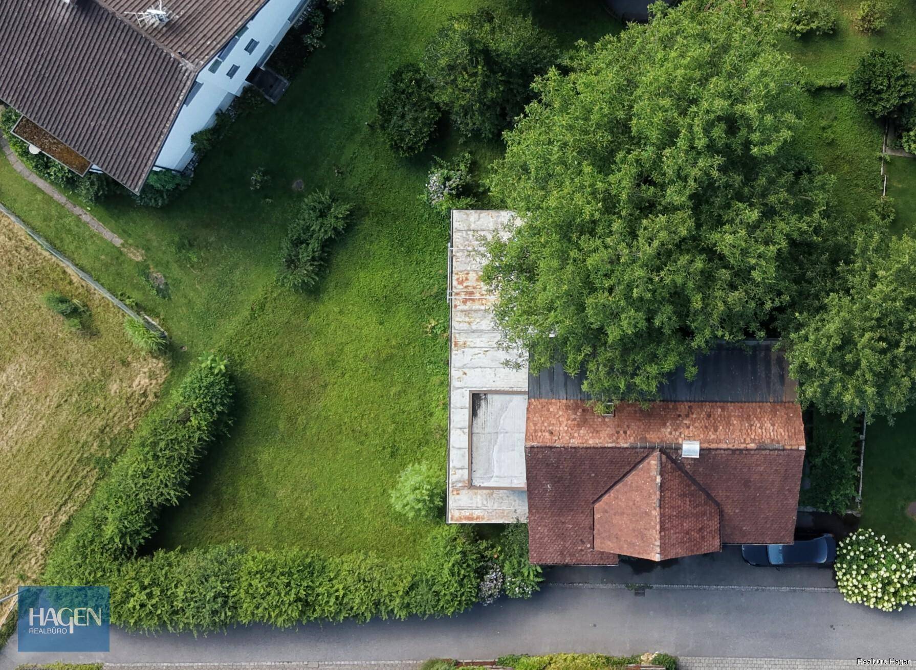 Direkte Draufsicht auf das Haus mit rotem Ziegeldach, umgeben von üppigem Grün und hohen Bäumen.