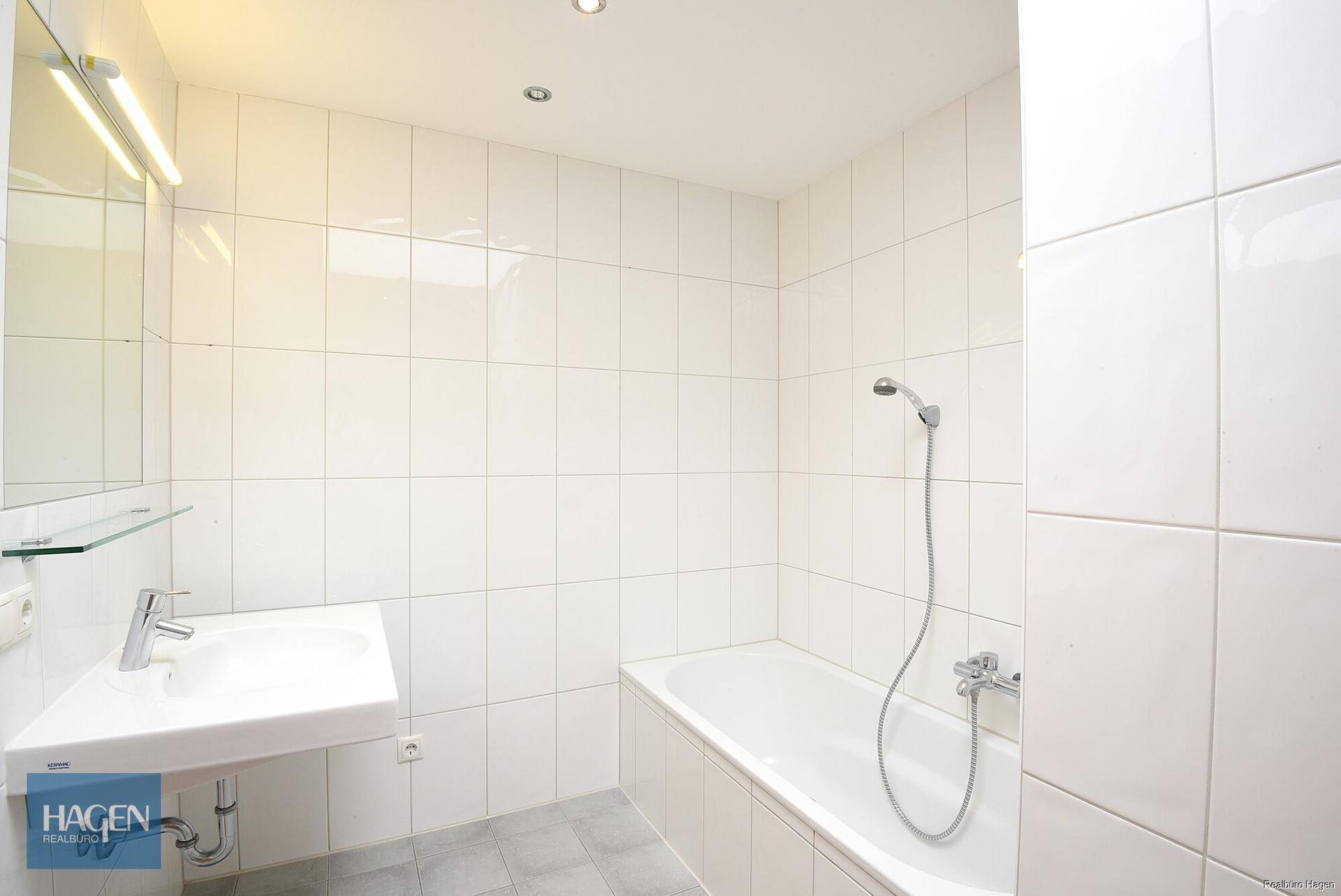 Modern gefliestes Badezimmer mit Badewanne, Duschfunktion und einem Waschbecken.