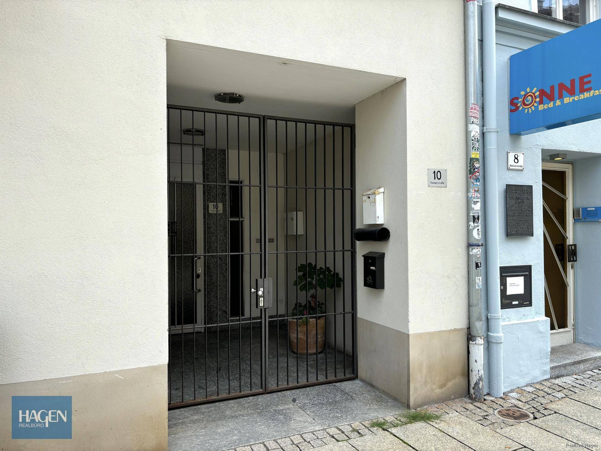 Eingangsbereich eines Mehrfamilienhauses mit Gittertür und Briefkästen.