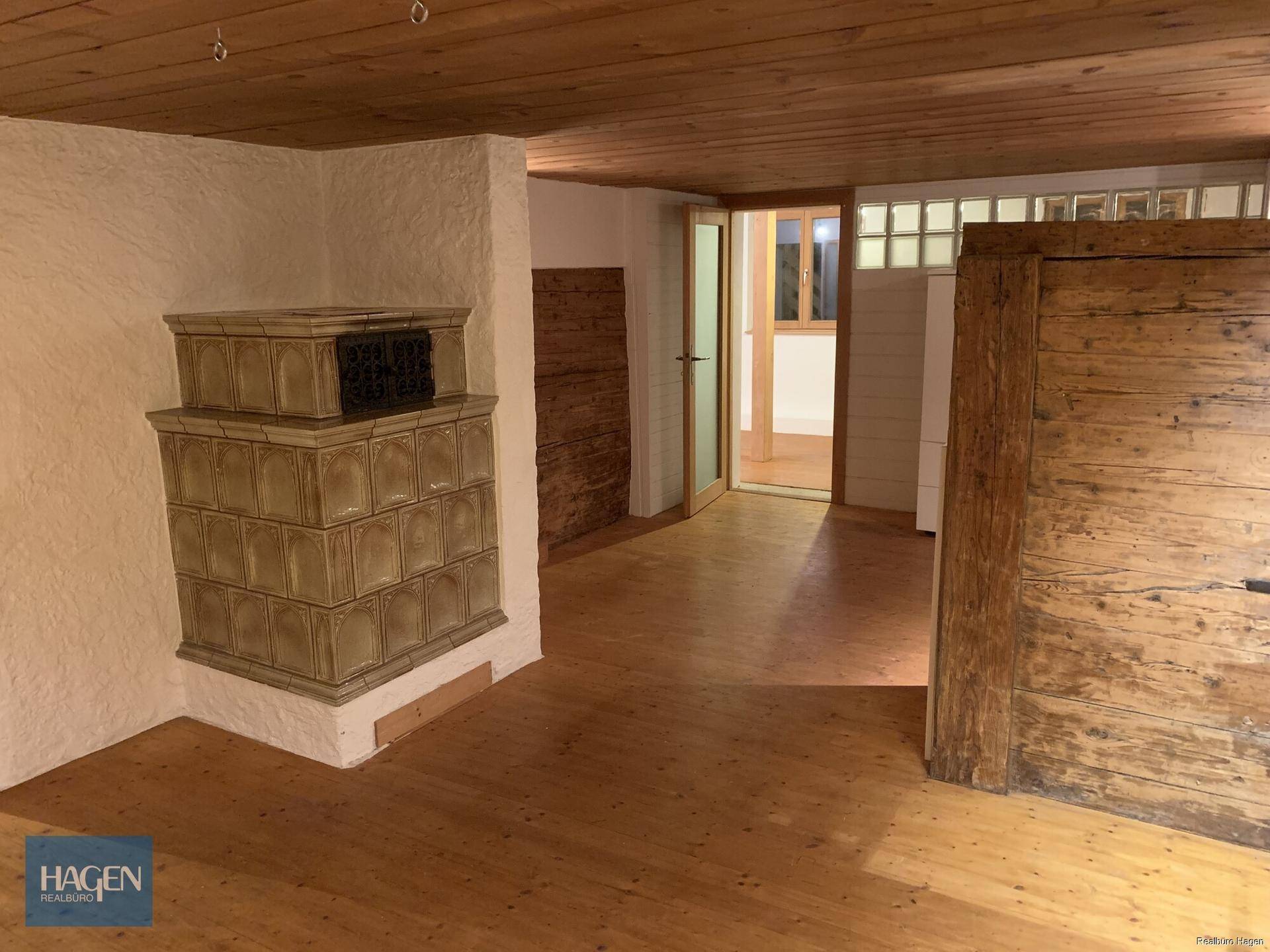 Offener Wohnbereich mit Holzboden, einem traditionellen Kachelofen und Holztüren.