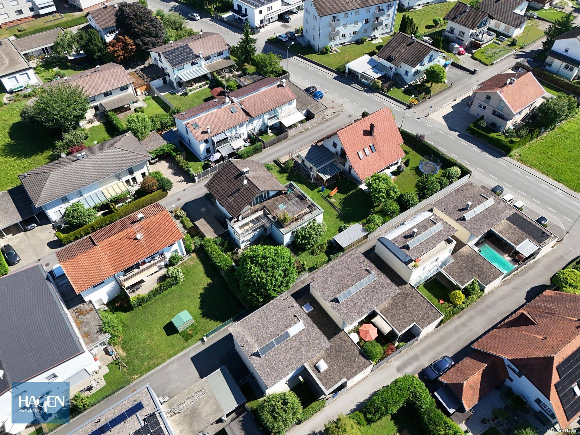 Luftaufnahme einer Wohnsiedlung mit Einfamilienhäusern, Gärten und Straßen in sonniger Umgebung.