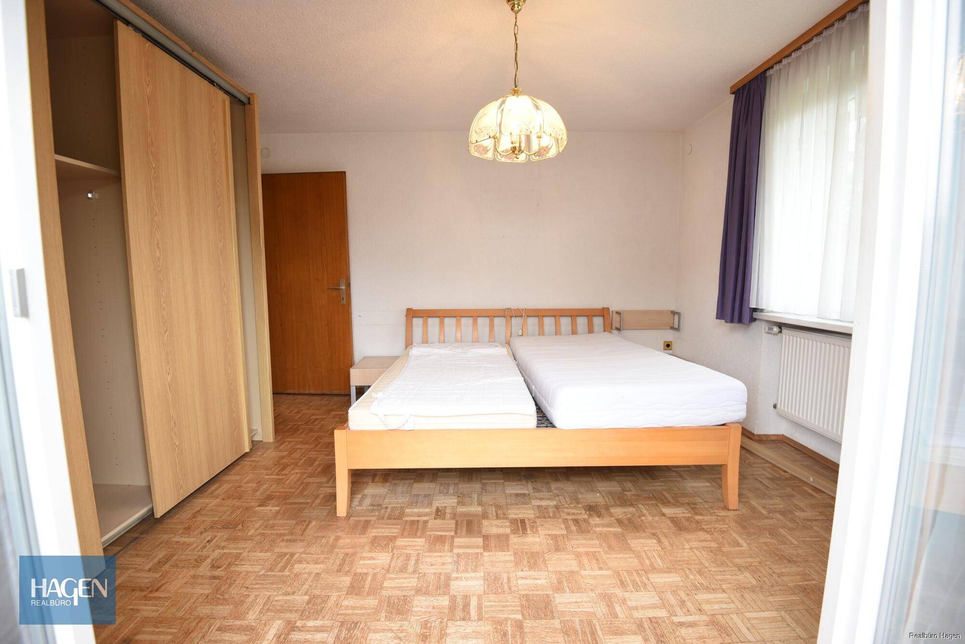 Schlafzimmer mit Parkettboden, Doppelbett und großem Einbauschrank.