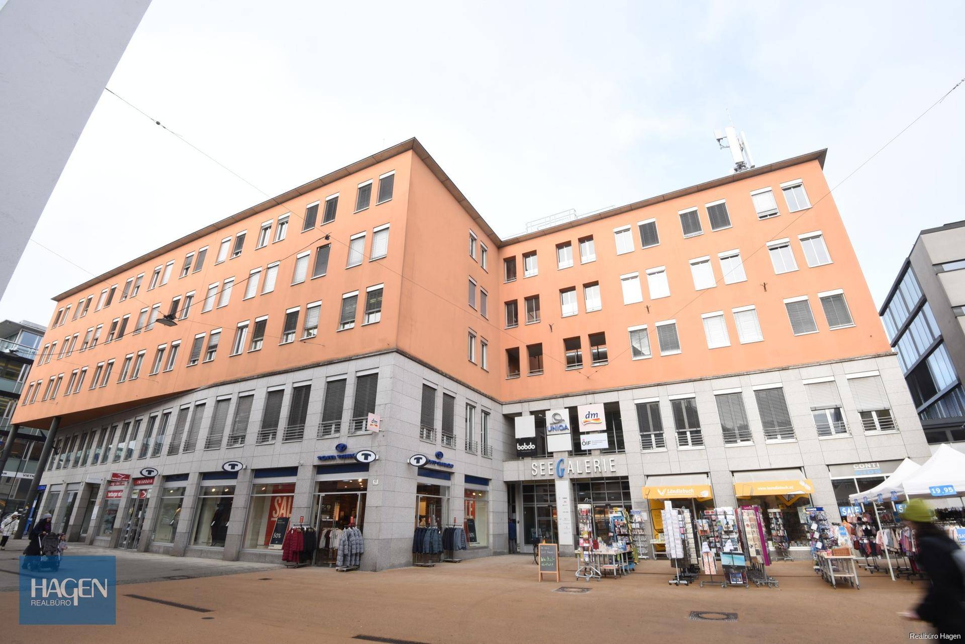 Mehrstöckiges Gebäude mit Geschäften im Erdgeschoss und Wohnungen darüber in urbaner Umgebung.