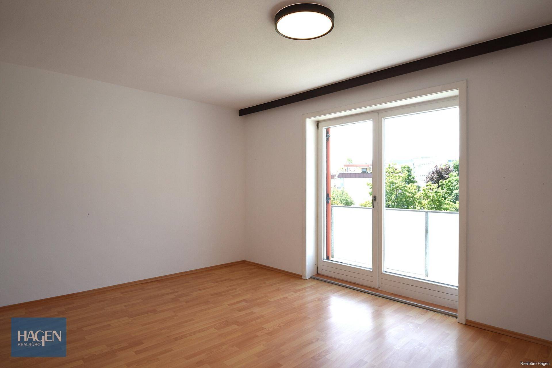 Helles Zimmer mit Laminatboden und Zugang zu einem französischen Balkon, der viel Licht hereinlässt.