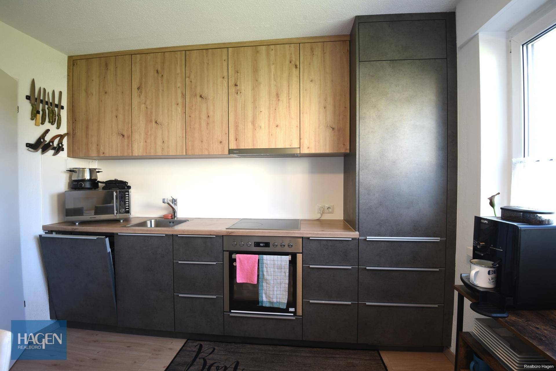 Einbauküche mit Holz- und Anthrazitfronten, Spüle, Kochfeld und integriertem Backofen.