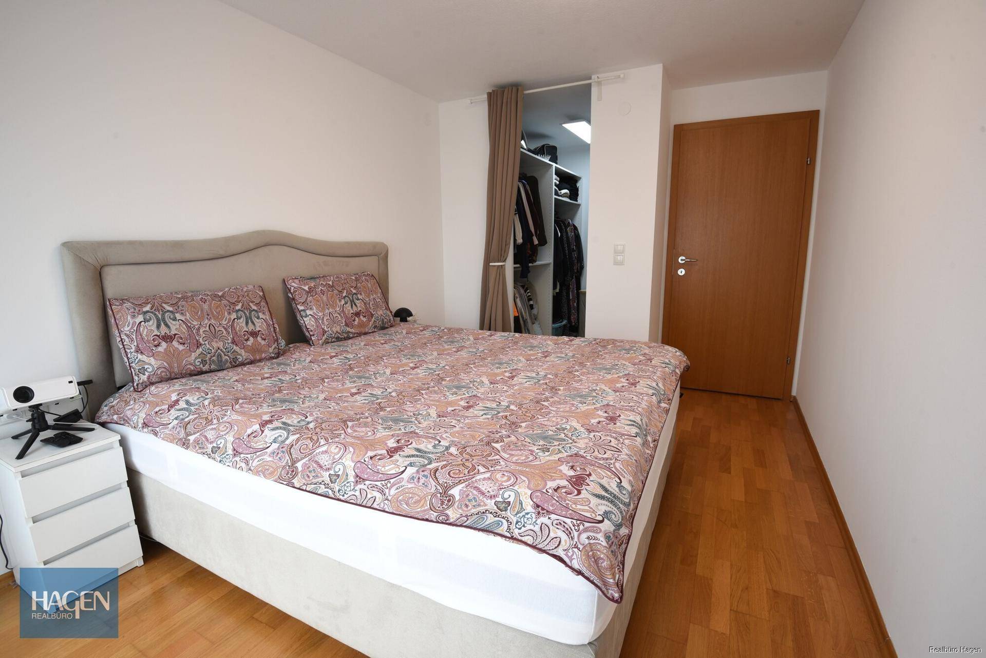 Schlafzimmer mit Doppelbett, Parkettboden und offenem Zugang zum begehbaren Kleiderschrank.