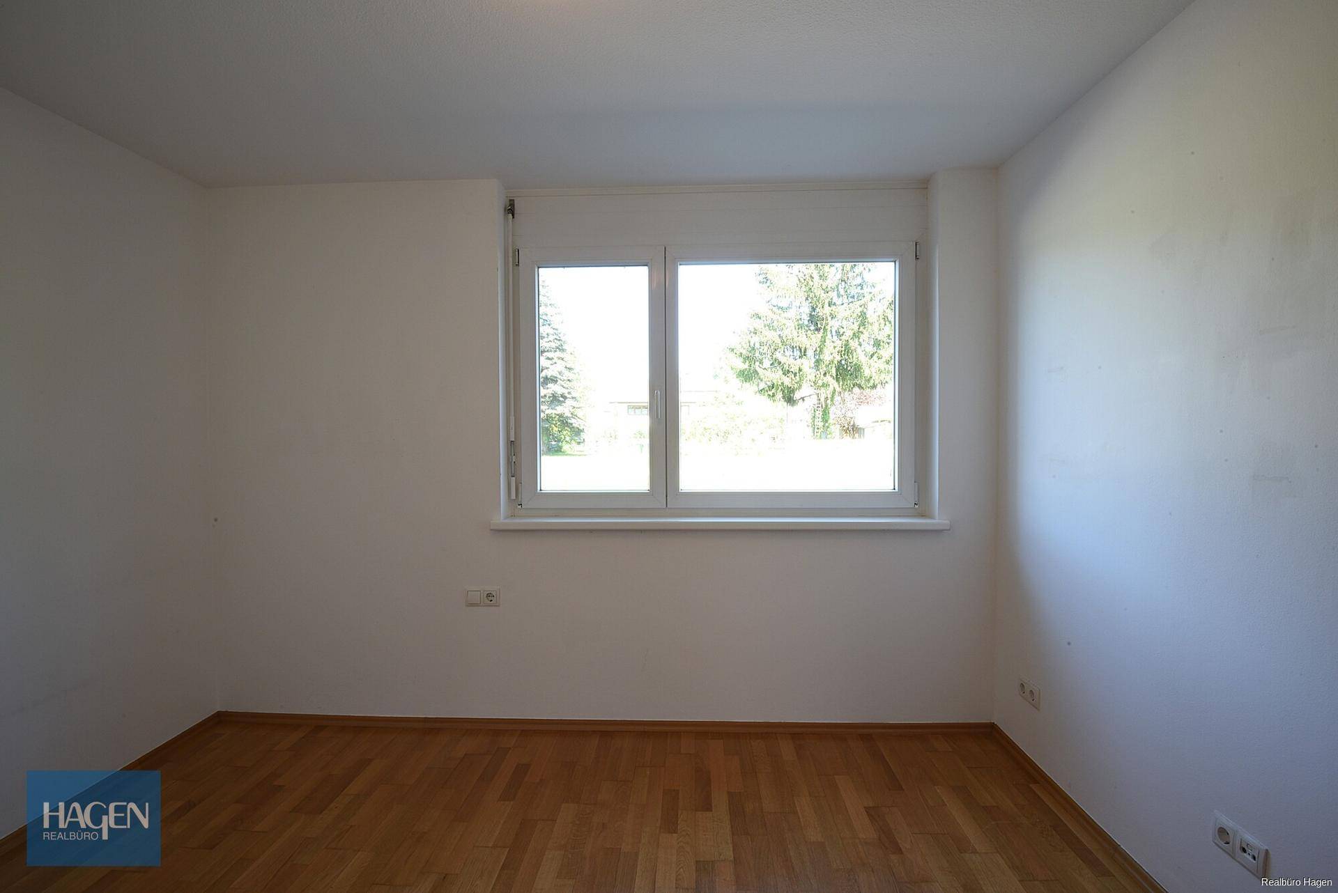 Helles Zimmer mit Parkettboden und Fenster mit Blick ins Grüne.