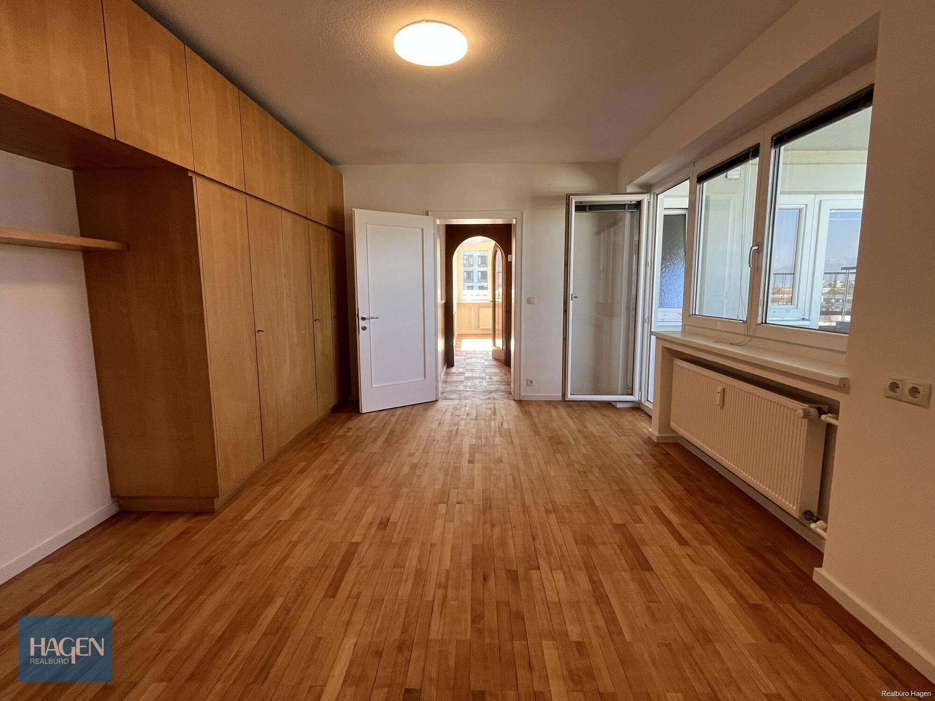 Geräumiges Schlafzimmer mit Holzboden, großen Einbauschränken und viel Tageslicht durch die Fensterfront.