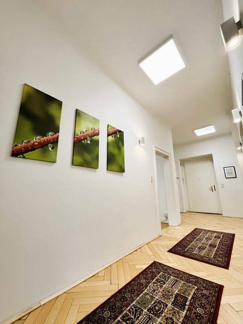 Langer Flur mit Fischgrätparkett, modernen Wandleuchten und dekorativen Bildern an der Wand.