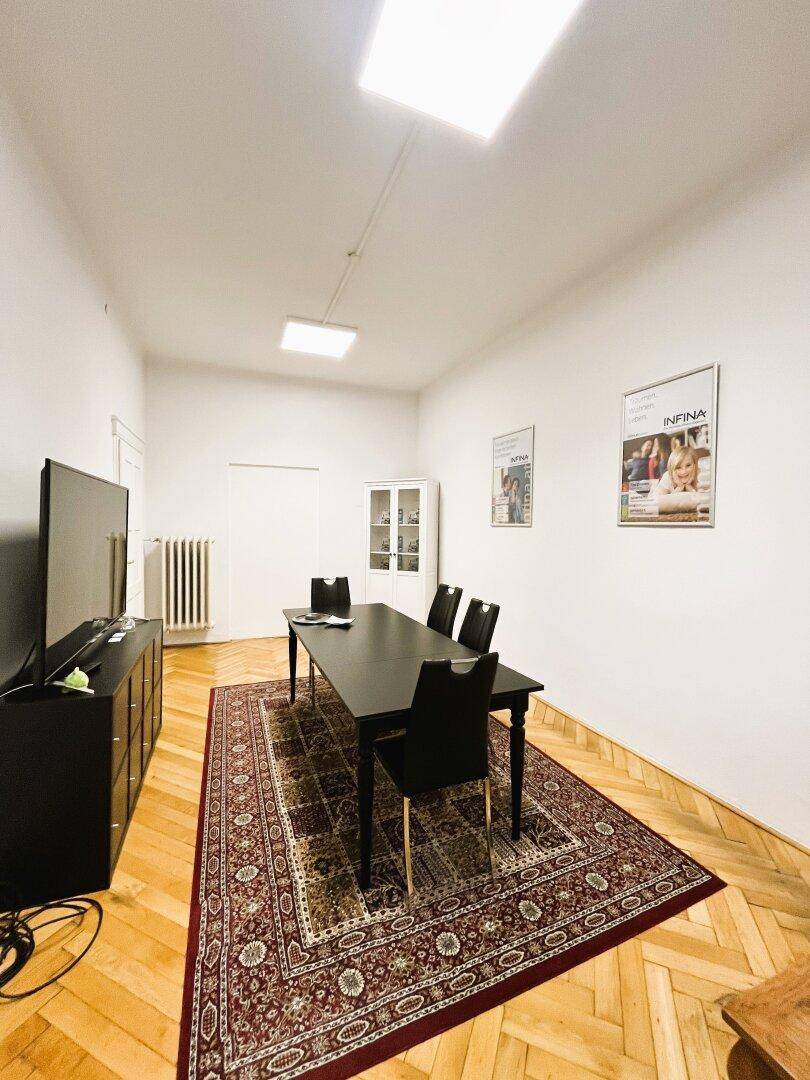 Geräumiger Büroraum mit Fischgrätparkett, einem großen Tisch und einem Vitrinenschrank im Hintergrund.