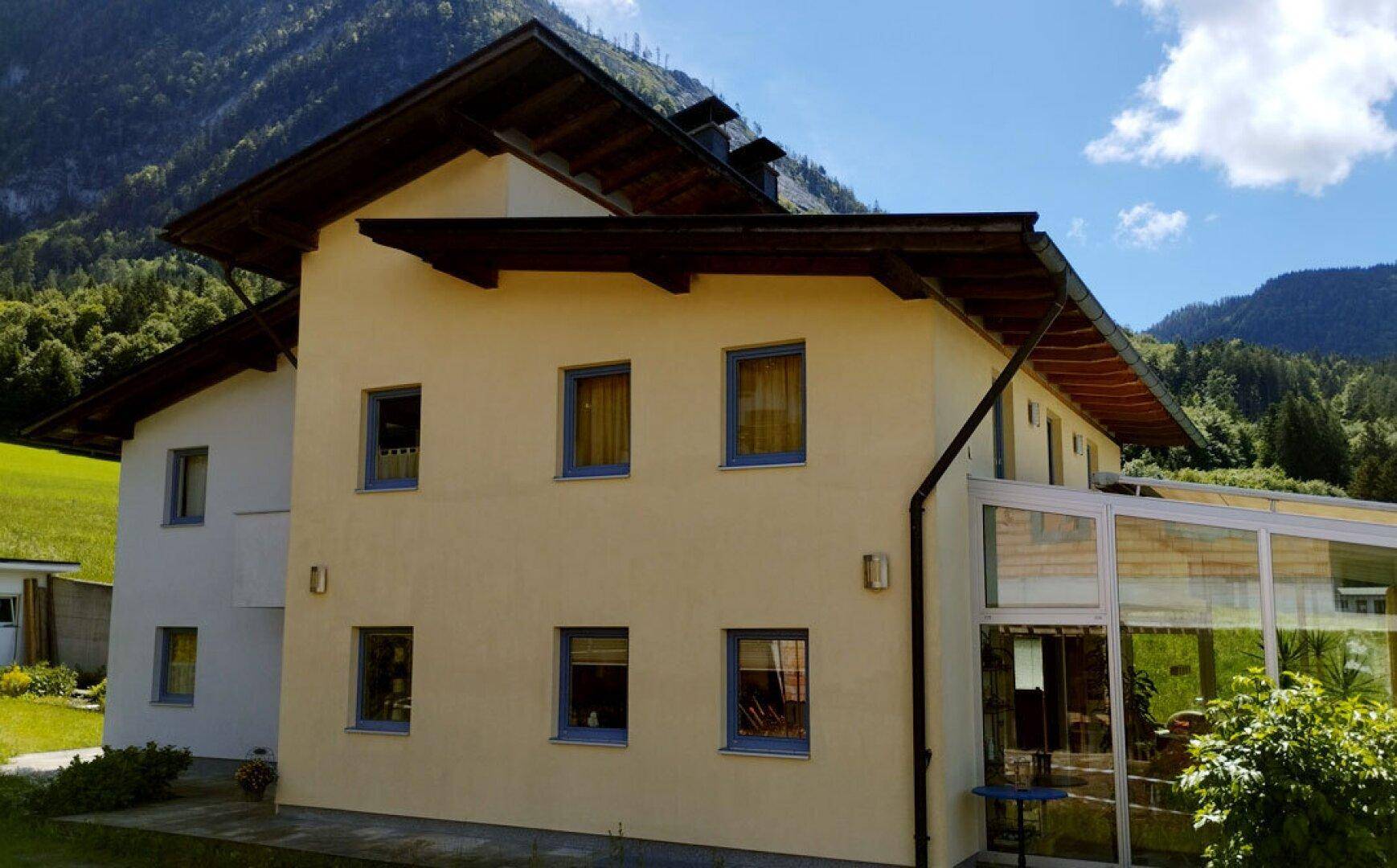 Seitenansicht des Hauses mit Wintergarten und grüner Berglandschaft im Hintergrund.