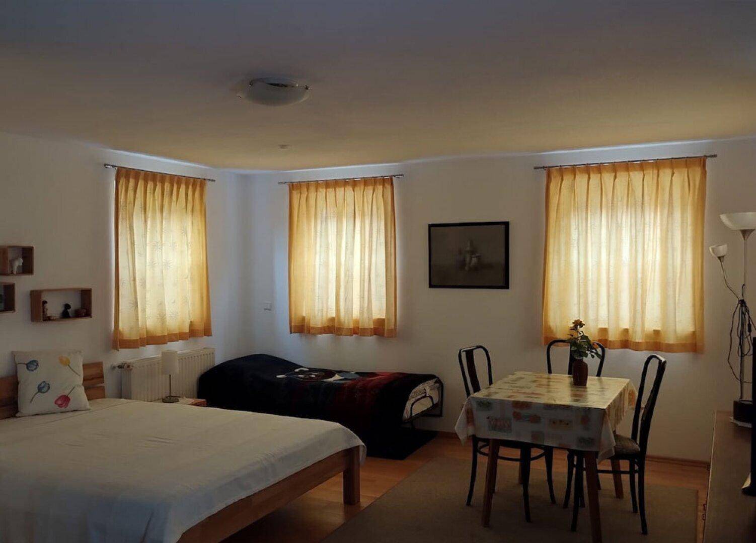 Gemütliches Schlafzimmer mit zwei Betten, kleinem Esstisch und hellen gelben Vorhängen.