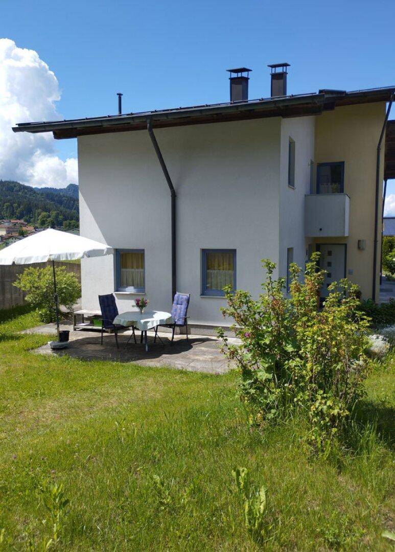 Hinterhof des Hauses mit kleiner Terrasse, Gartenmöbeln und Rasenfläche.