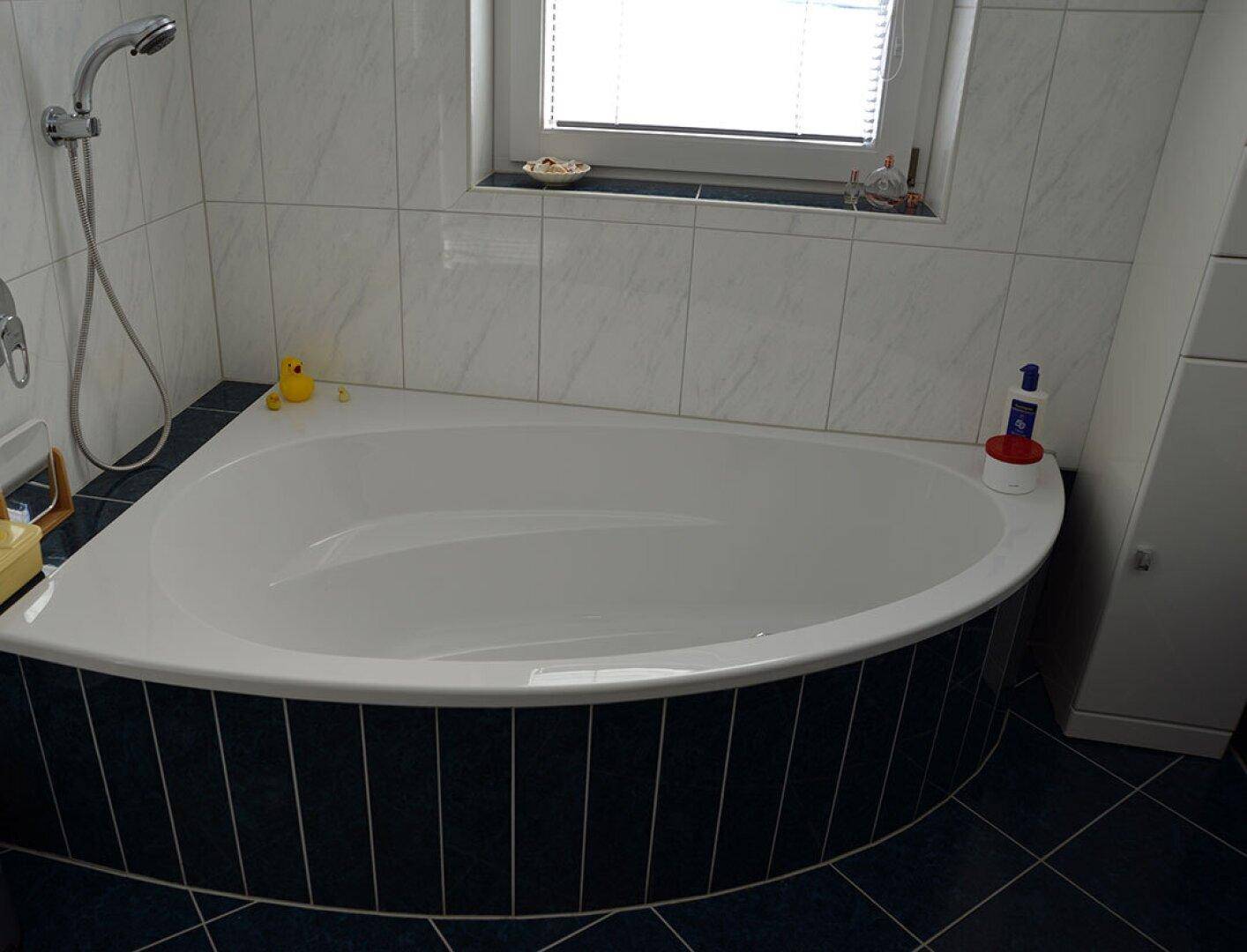 Badezimmer mit Eckbadewanne und weiß-blauen Fliesen, die eine entspannende Atmosphäre bieten.