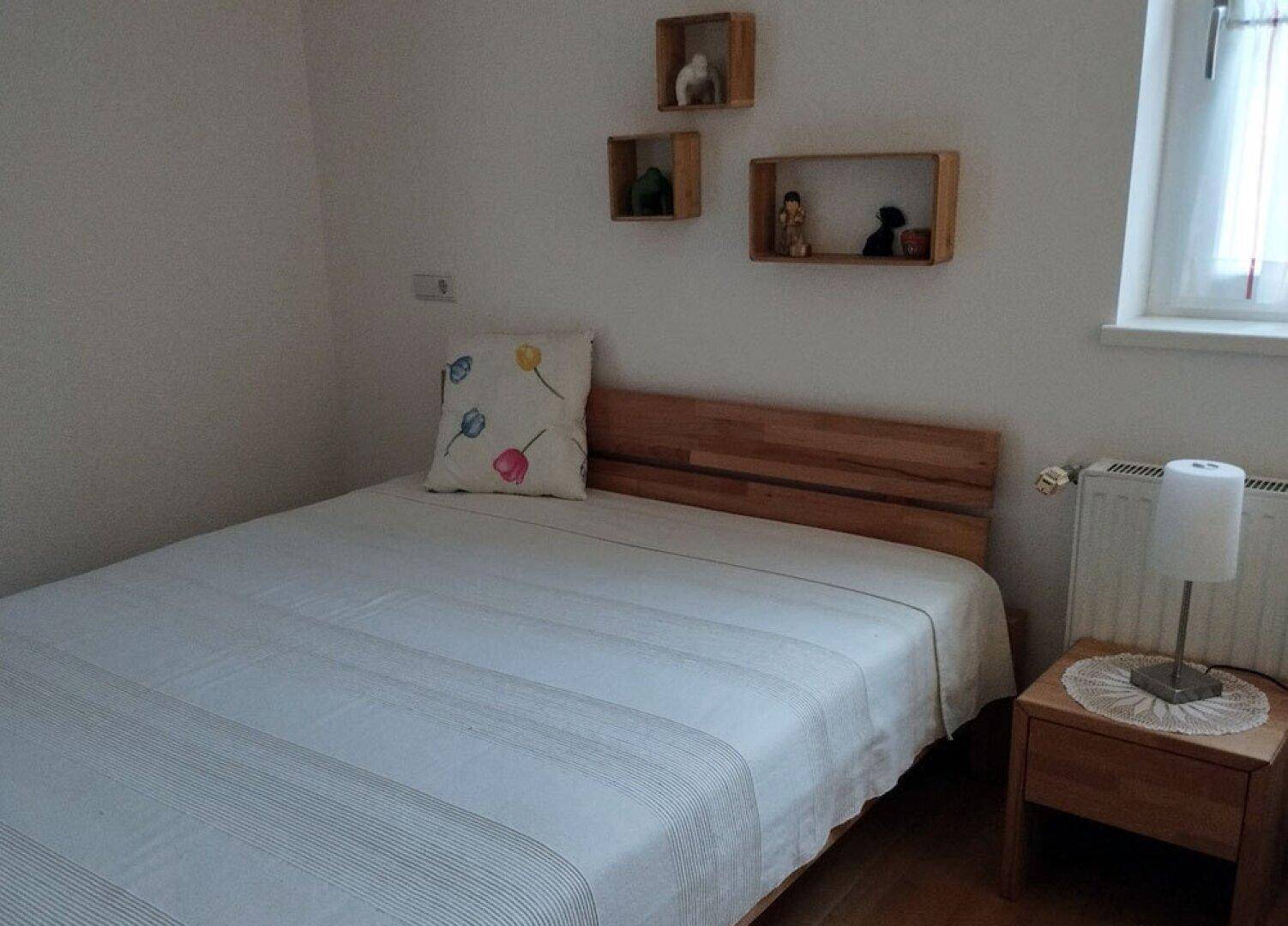 Gemütliches Schlafzimmer mit Holzbett, Nachttisch, Heizkörper und kleinem Fenster.
