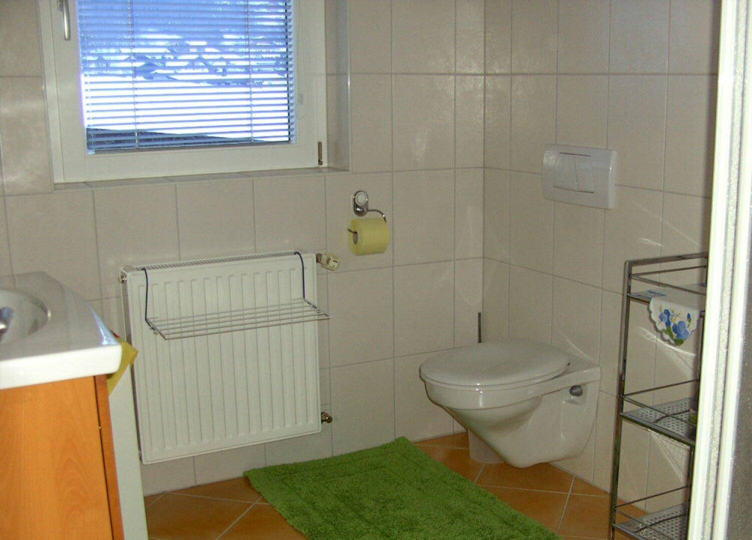 Helles Badezimmer mit WC, Waschbecken, Heizkörper und Fenster, gefliest in neutralen Farben.