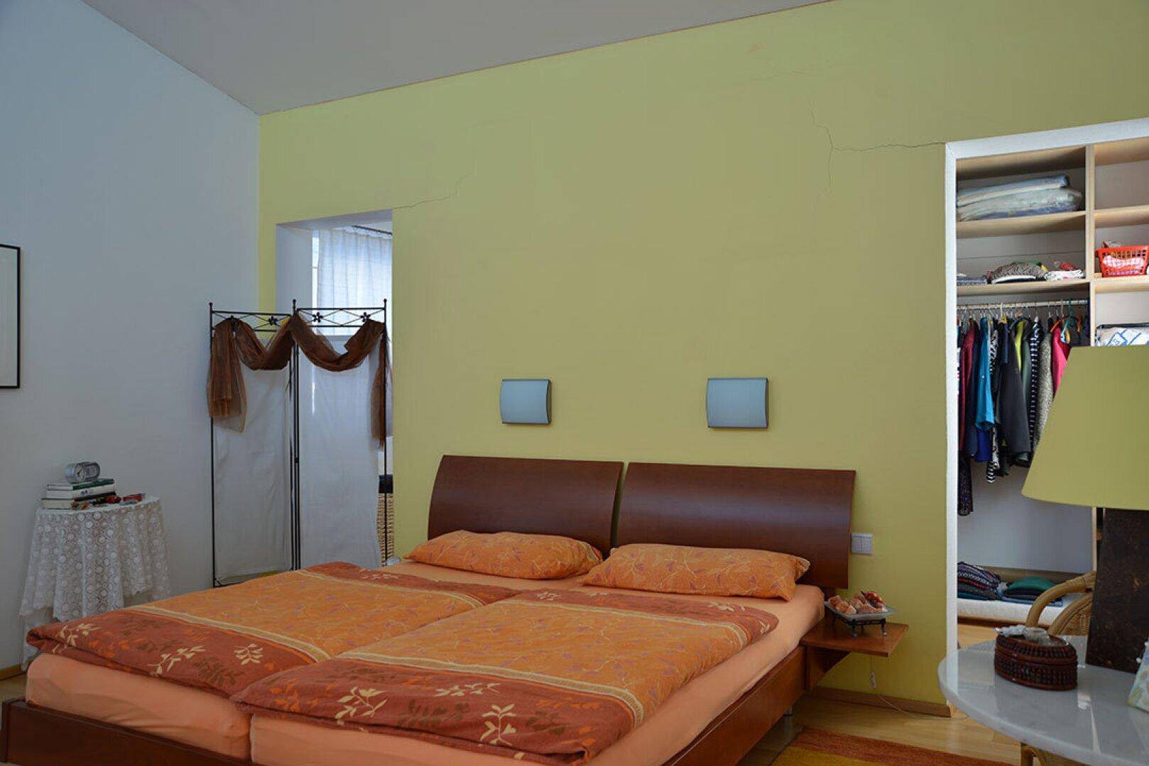 Schlafzimmer mit Doppelbett, gelben Wänden und offenem Kleiderschrankbereich für viel Stauraum.