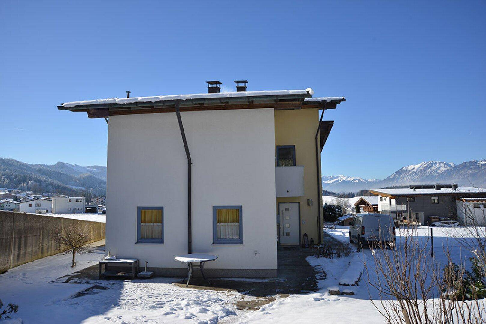 Rückansicht des Hauses im Winter mit Schnee und verschneiten Bergen in der Ferne.