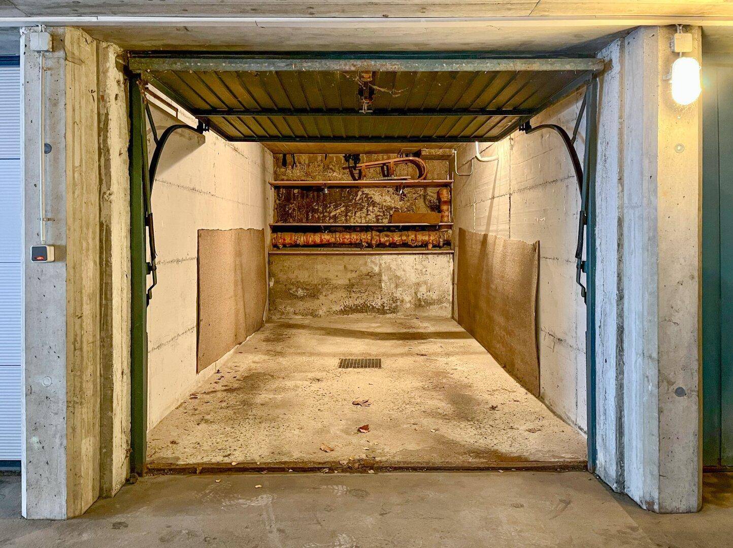 Leere Einzelgarage mit Betonwänden und einem aufklappbaren Garagentor.