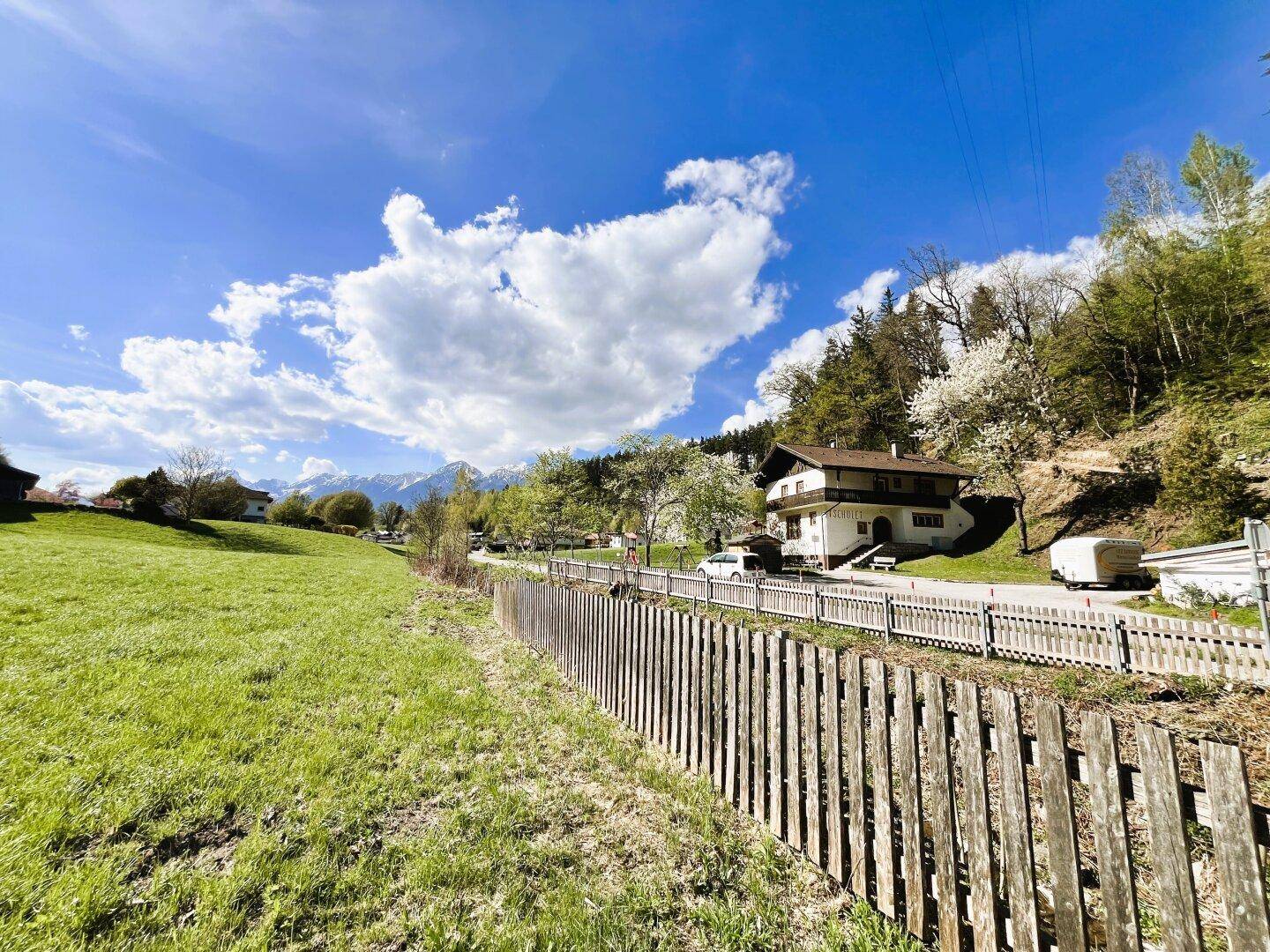 Ländliche Umgebung mit einem Wohnhaus, Holzzaun und weitem Blick auf die Berglandschaft.