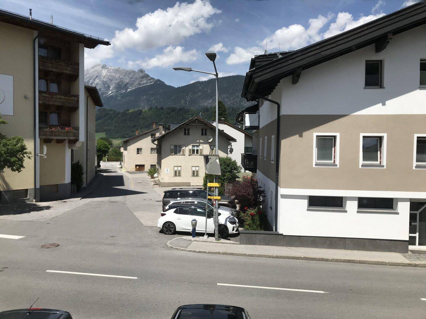 Straßenansicht mit geparkten Autos und Häusern, im Hintergrund majestätische Berge.
