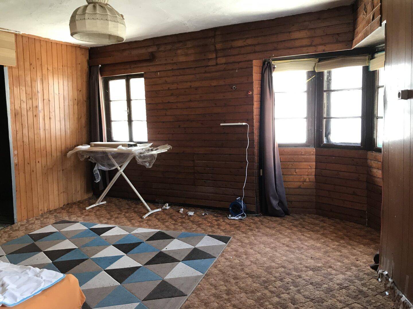 Schlafzimmer mit Holzvertäfelung, Teppichboden und zwei Fenstern.