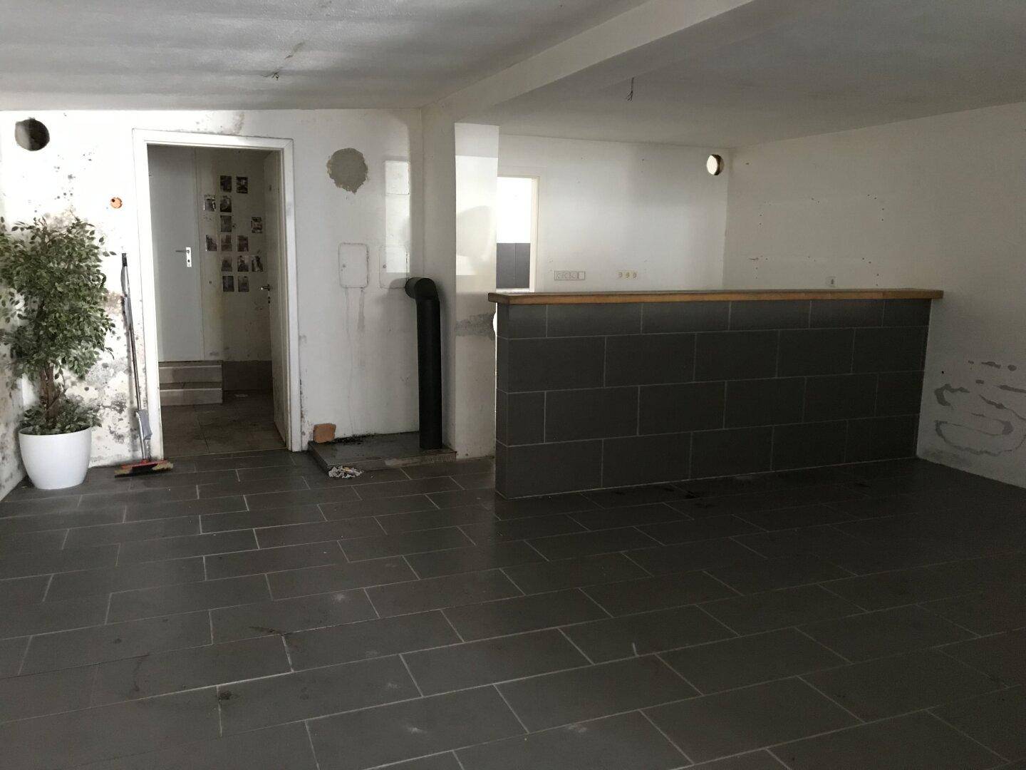 Großer Raum mit grauen Fliesen und einer Theke, möglicherweise für einen Barbereich.
