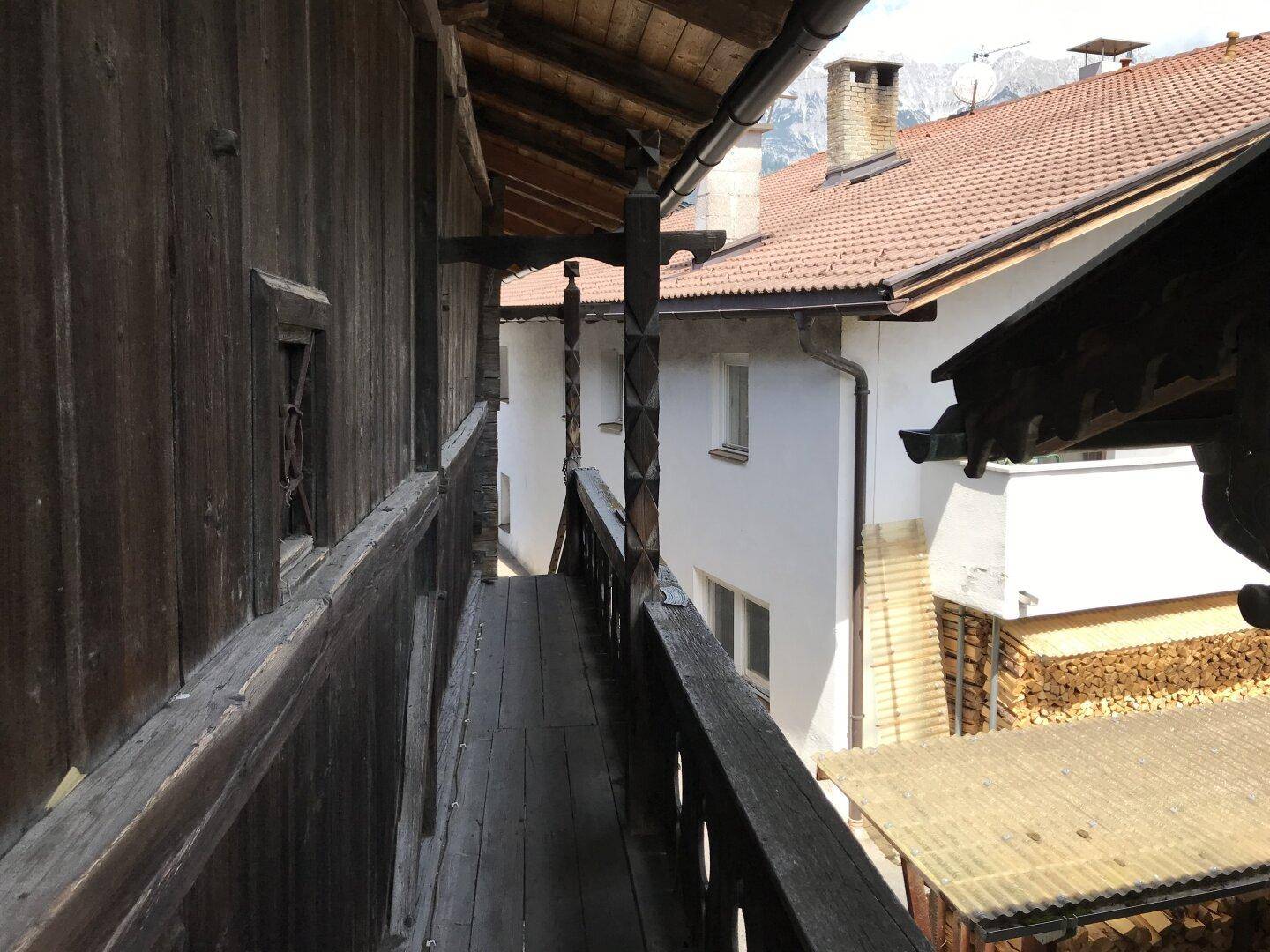 Traditioneller Holzbalkon mit Blick auf benachbarte Dächer und gestapeltes Brennholz.