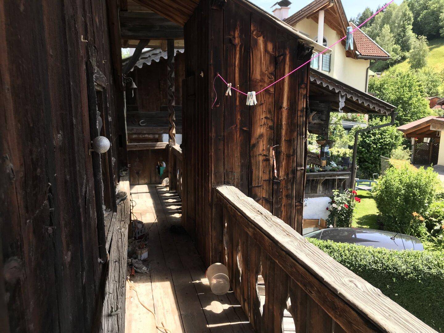 Alter Holzbalkon mit Wäscheleine und Blick auf den Garten und die Nachbarschaft.