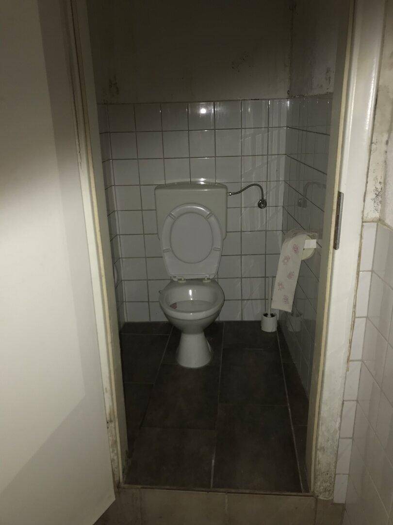 Kleines WC mit weißen Fliesen und einer einfachen Toilette.