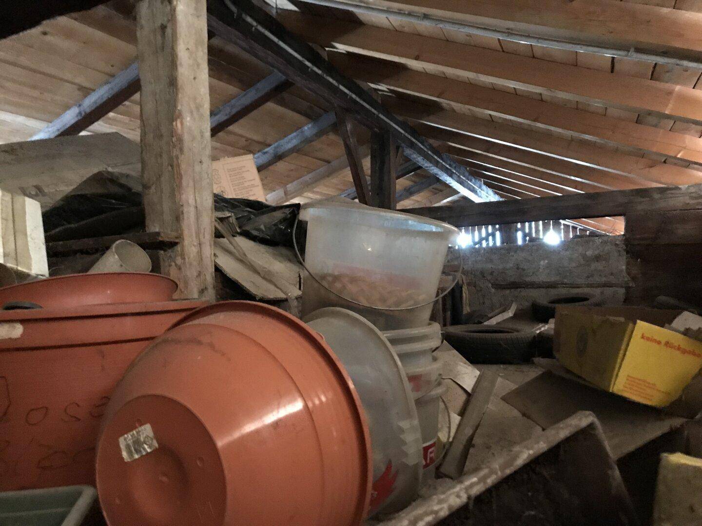Unausgebauter Dachboden mit sichtbaren Holzbalken und verschiedenen gelagerten Gegenständen.