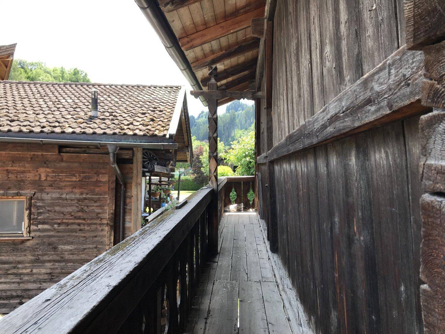 Langer, schmaler Holzbalkon mit Blick auf grüne Bäume und die umliegende Natur.