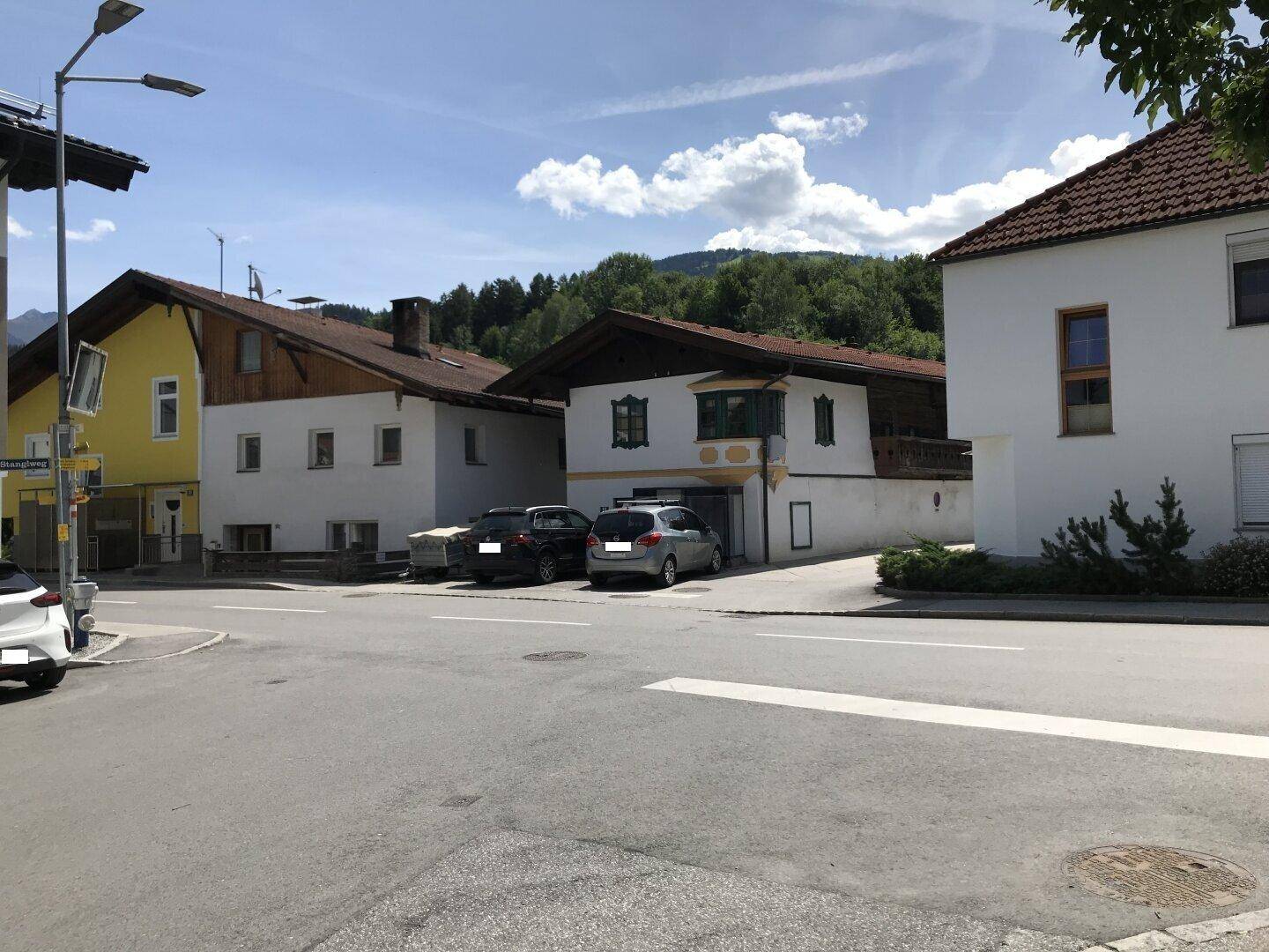 Wohngebäude an einer Straße mit geparkten Autos und Bergblick im Hintergrund an einem sonnigen Tag.