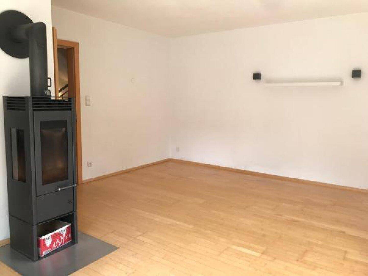 Helles Wohnzimmer mit hellem Holzboden und einem modernen Holzofen als Wärmequelle.