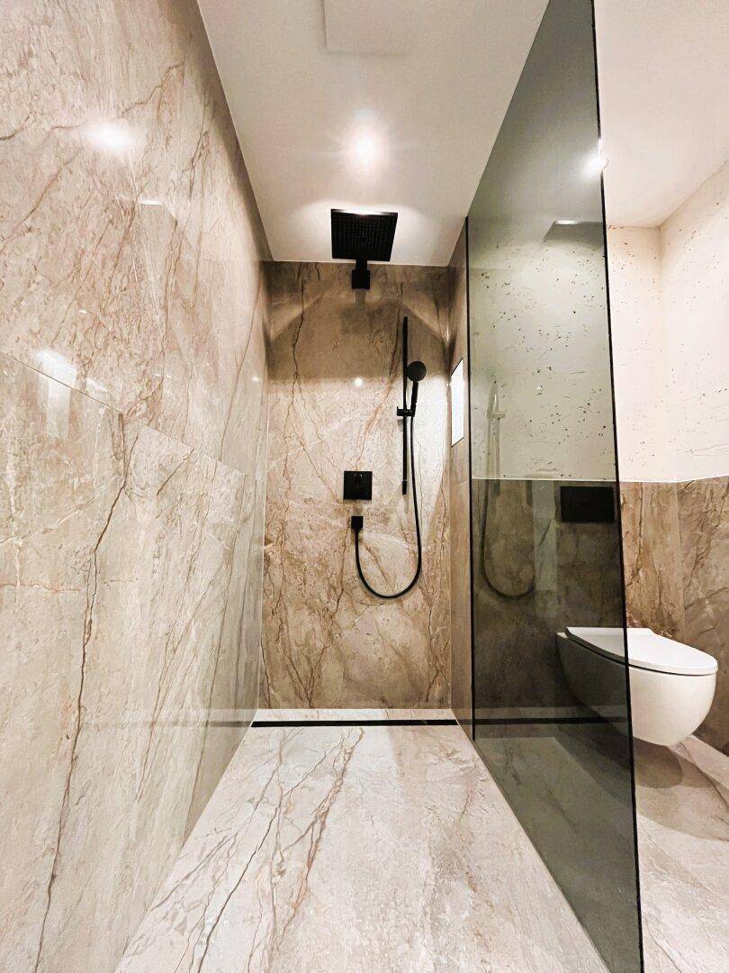 Modernes Badezimmer mit begehbarer Regendusche und wandhängendem WC, verkleidet mit Marmorfliesen.