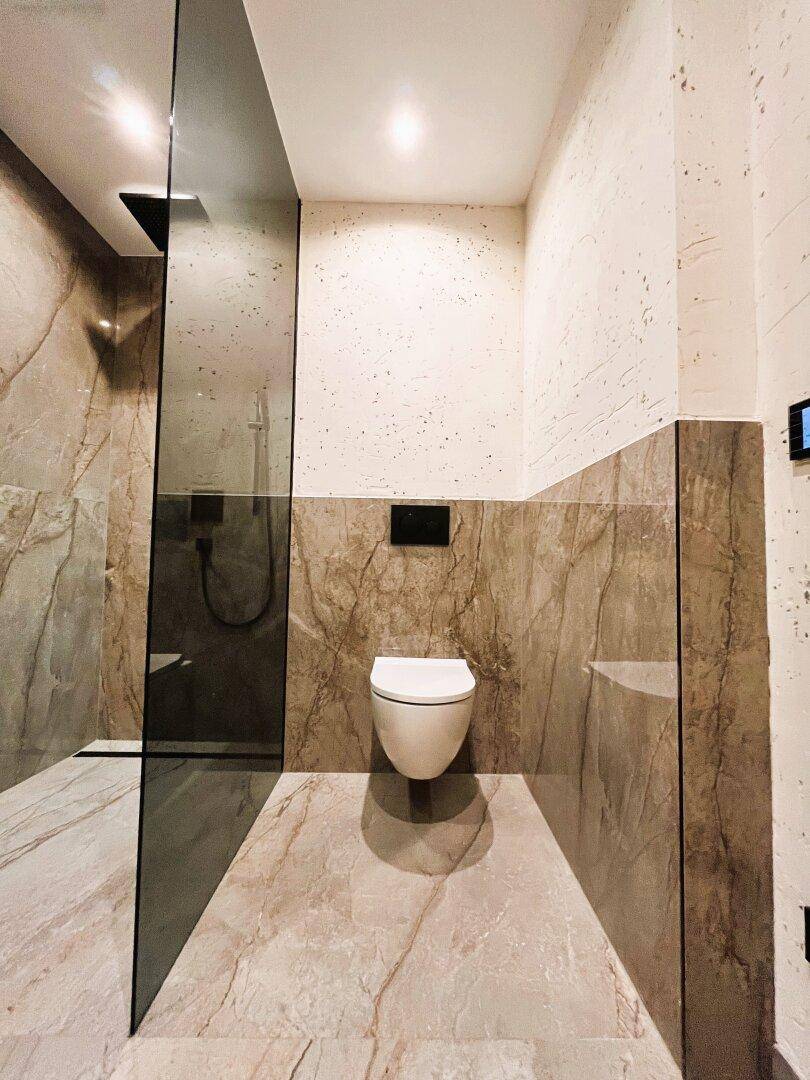 Modernes Badezimmer mit wandhängendem WC und eleganten Marmorfliesen an Wänden und Boden.