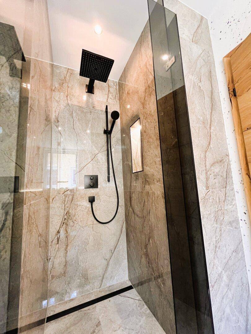 Elegantes Badezimmer mit begehbarer Regendusche und hochwertigen Marmorfliesen.