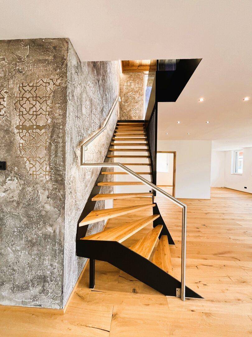 Moderne Holztreppe mit Metallgeländer und einer kunstvoll gestalteten Wandverkleidung.