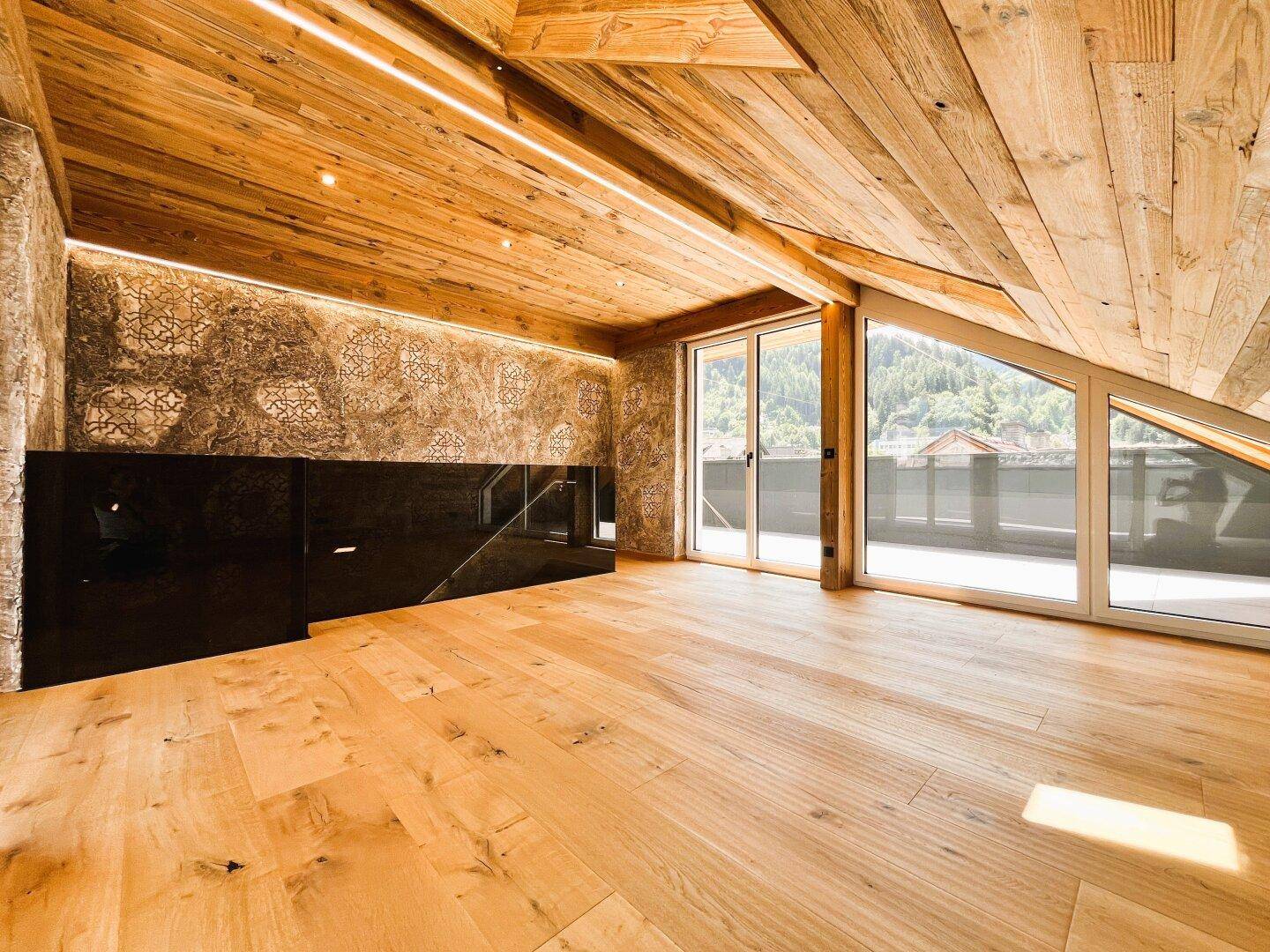 Heller Dachraum mit Holzboden und Holzdecke, großen Fenstern und Bergblick.