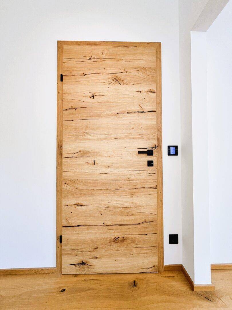 Massive Holztür mit markanter Maserung und modernem schwarzem Türgriff.